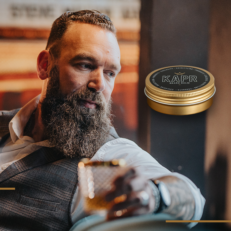 Open blik KAPR baardbalsem met gladde balsem erin.|Premium Beard Balm 60ml blik geplaatst tegen een luxueuze donkere achtergrond.|Een man met baard en een blik Beard Balm in een luxueuze setting|Blik Premium Beard Balm 60ml met de belangrijkste productvoordelen uitgelicht (zachte en soepele baard, verzorgend en voedend, flexible hold & shine).