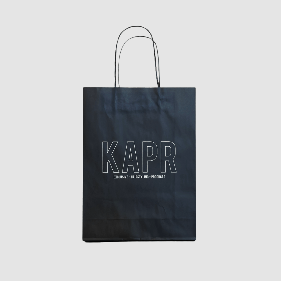 KAPR tas – zwarte papieren tas met wit logo op grijze achtergrond, luxe draagtas voor producten.