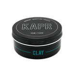model met een strakke en matte look.|KAPR haarklei- Luxe zwarte kleiverpakking tegen een stijlvolle donkere achtergrond.||KAPR Clay 60ml met eigenschappen zoals extreme hold en verfrissende geur.