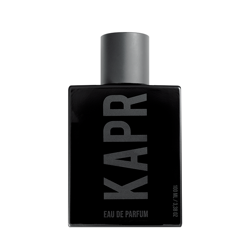 Mannelijk model met een stoere uitstraling gebruikt KAPR product.|KAPR exclusive Geur 50ml - Belangrijkste Geurkenmerken|KAPR Luxe Geur 2ml flesje met de tekst 'Eau de Essence'.|KAPR Luxe Parfum 50ml Fles en Doos - Eau de Parfum