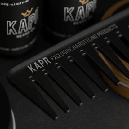 KAPR kam – zwarte stylingkam met logo tussen KAPR haarproducten, barbershop setting.