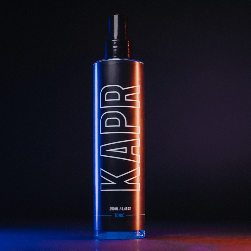 KAPR Tonic – zwarte fles met oranje-blauwe gloed, modern barbershop design.